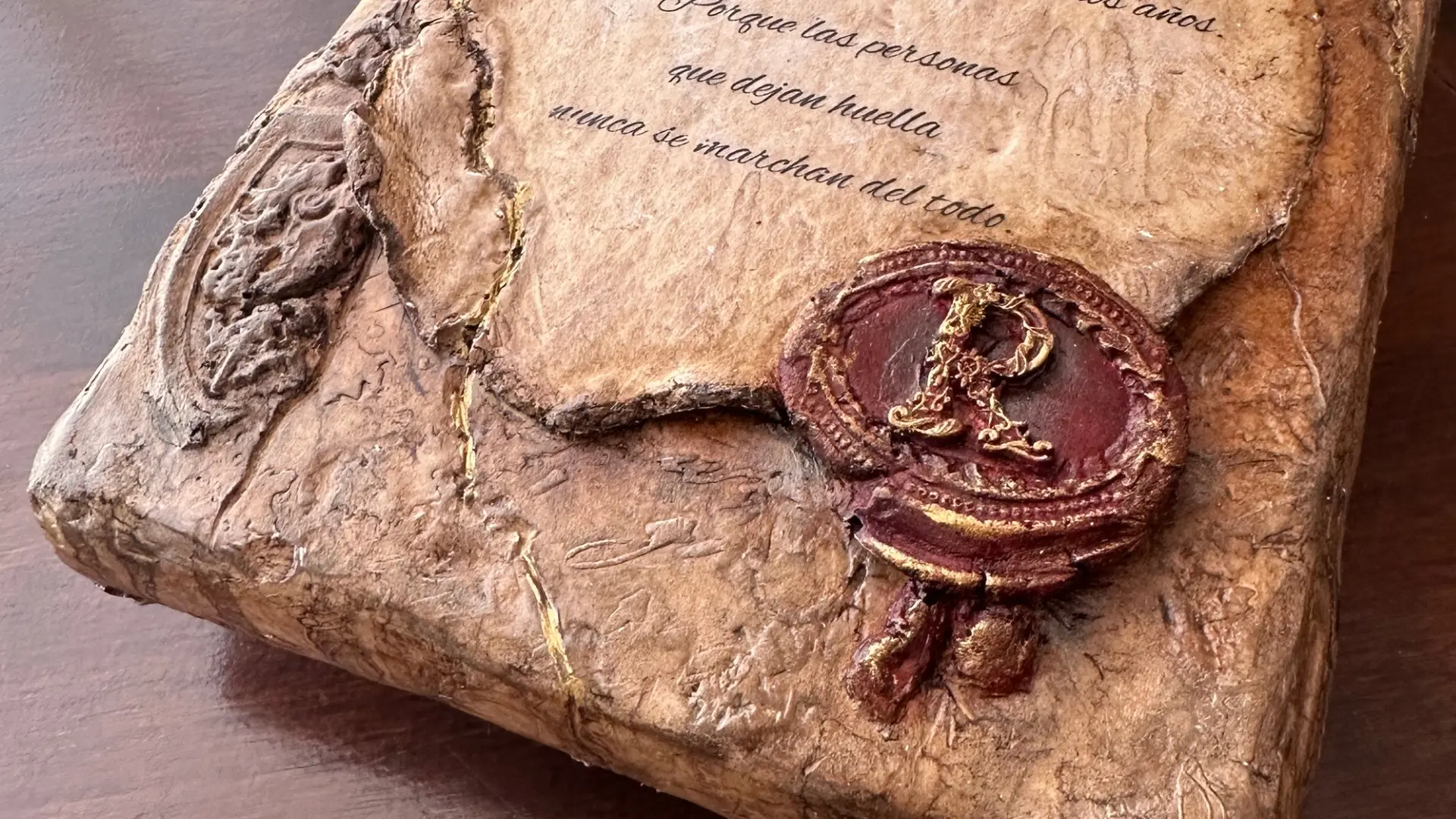 Detalle del sello burdeos, el pergamino y los relieves con acabados dorados de Ánima Scripta.